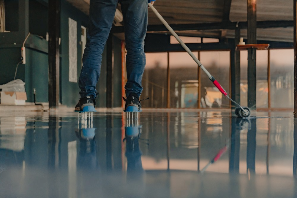 A man is painting a concrete floor with a roller.