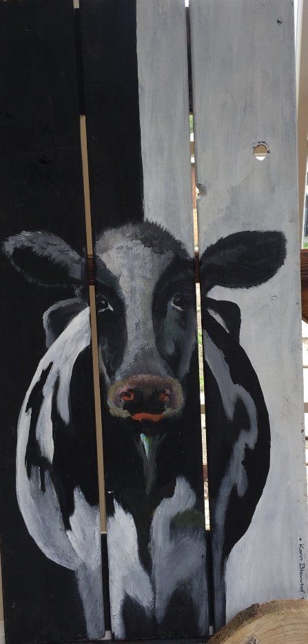 Een schilderij van een koe op drie verticale houten planken, met een zwarte achtergrond aan de linkerkant en een witte achtergrond aan de rechterkant.