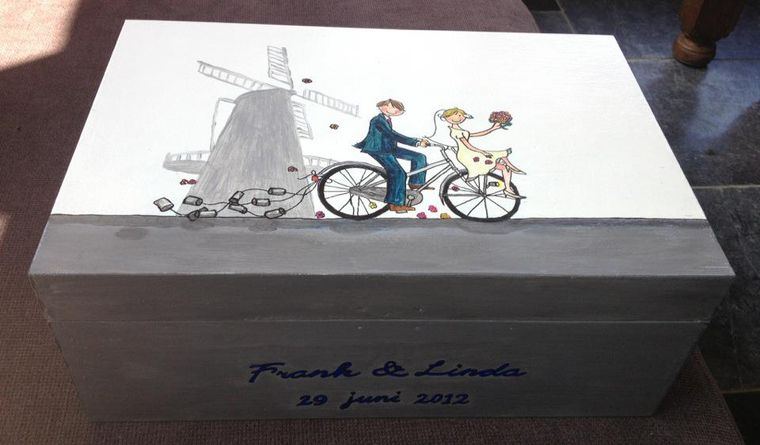 Een houten bewaardoos toont een stel op een fiets voor een windmolen, met de opschriften 