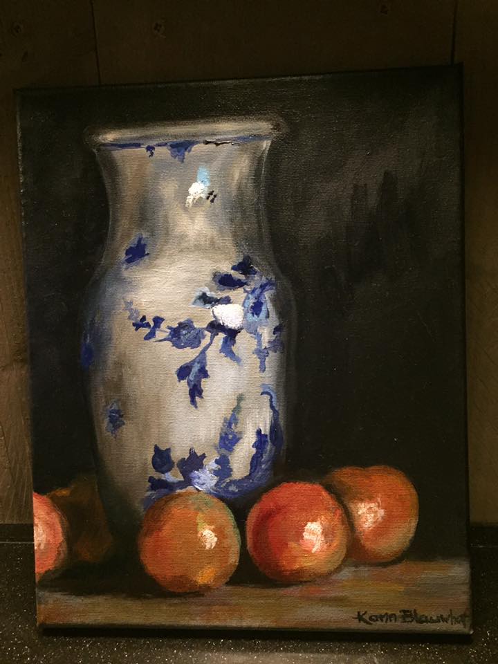Stilleven van een blauw-witte vaas met bloemen, omringd door sinaasappels, op een donkere, schaduwrijke achtergrond.