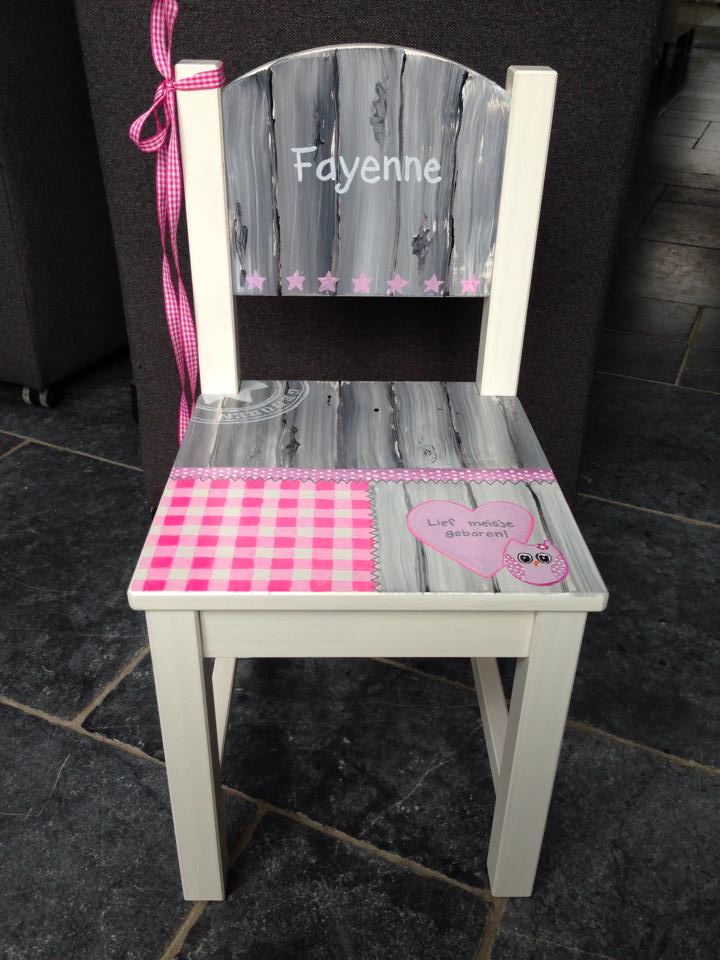 Een houten kinderstoel, grijs en wit geverfd, met een roze ruitjespatroon, een hartvormige versiering en de naam 
