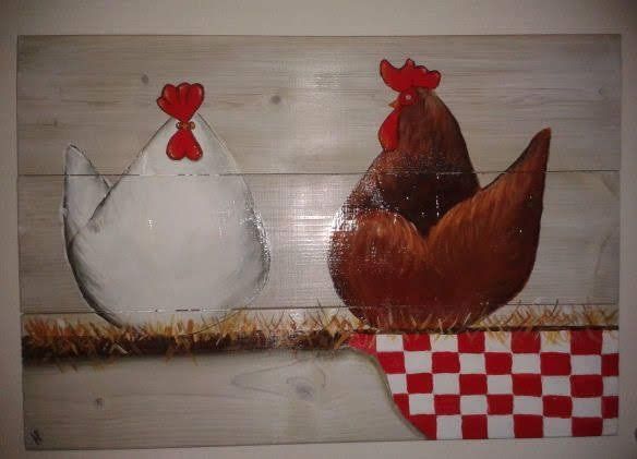 Een witte hen en een bruine haan staan ​​op stro boven een rood-wit geblokt patroon op een achtergrond van lichte houten planken.