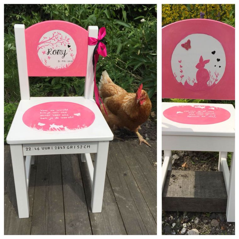 Een witte kinderstoel met een roze rugleuning en zitting, voorzien van gepersonaliseerde stickers, staat buiten naast een kip.