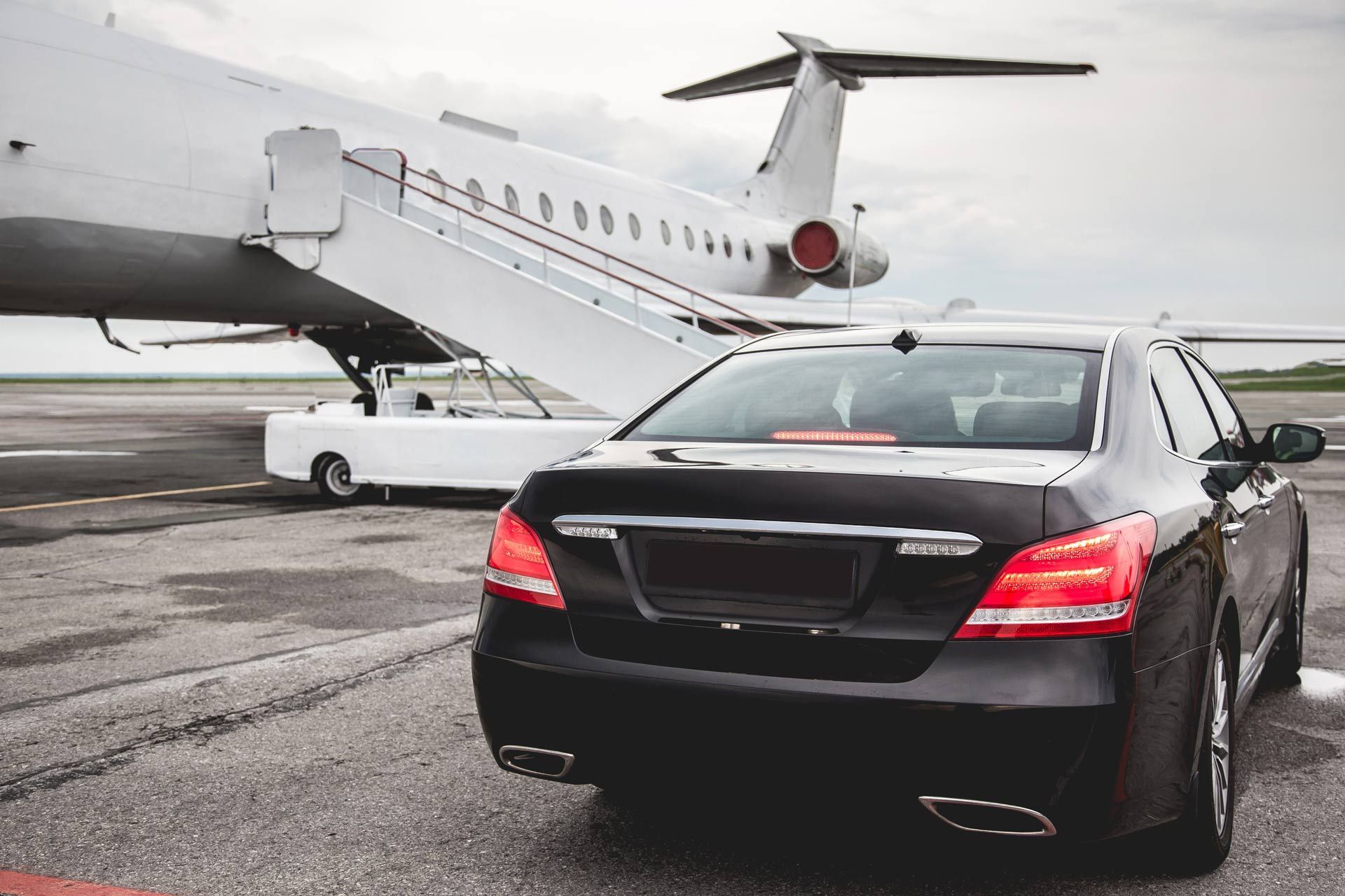 Black sedan parked on an airport tarmac near a private jet.