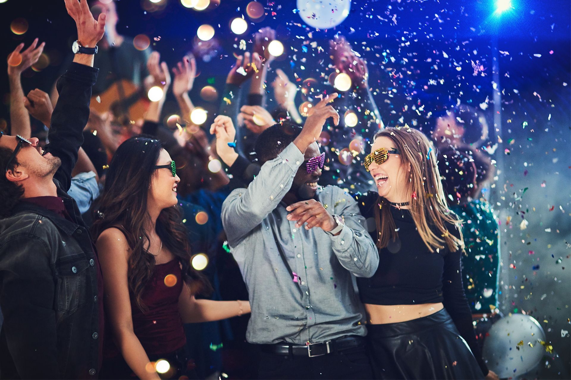 People dancing at a party with confetti and lights in the air.
