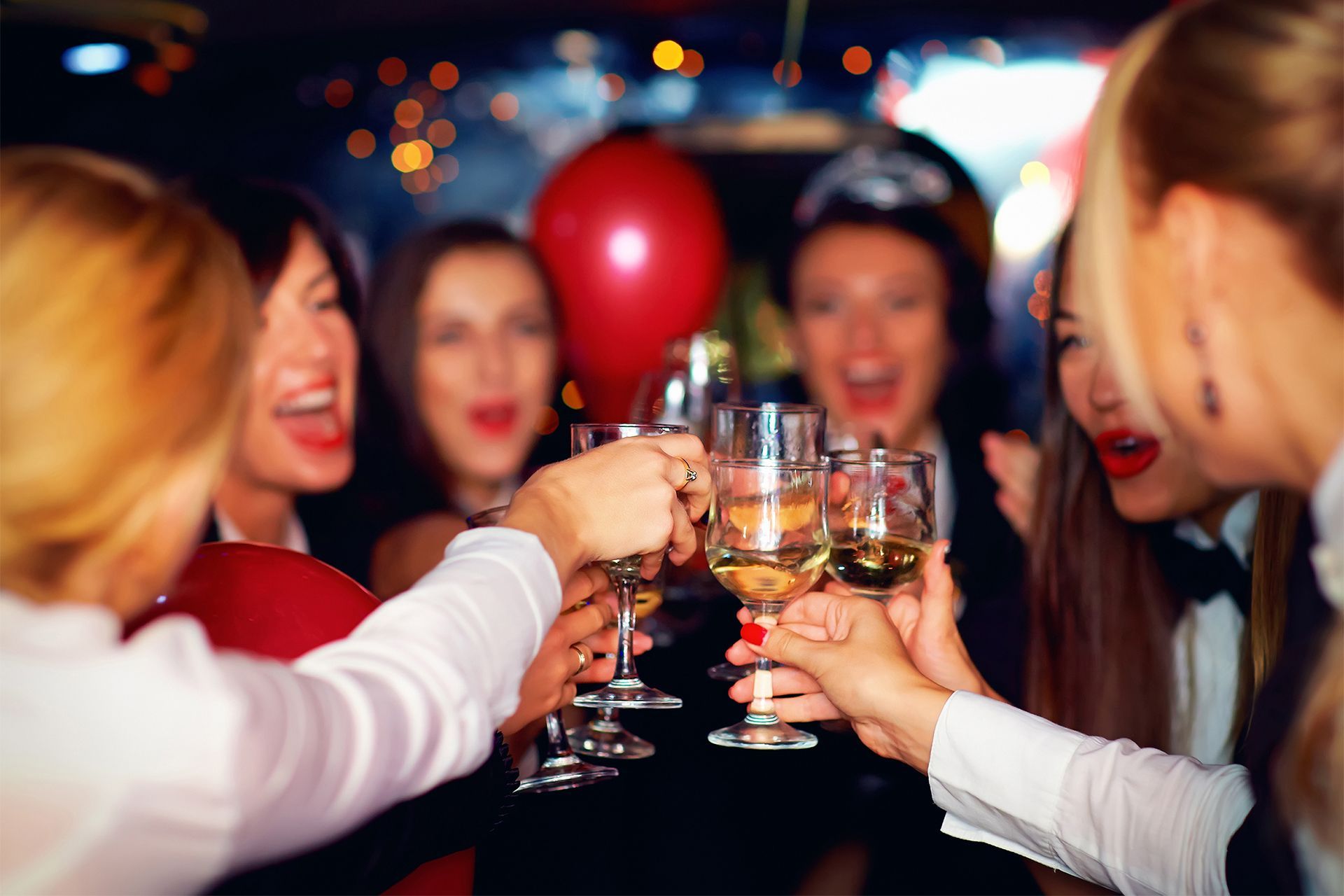 Women in formal attire toasting with champagne glasses at a party, celebratory smiles and a red balloon in the background.
