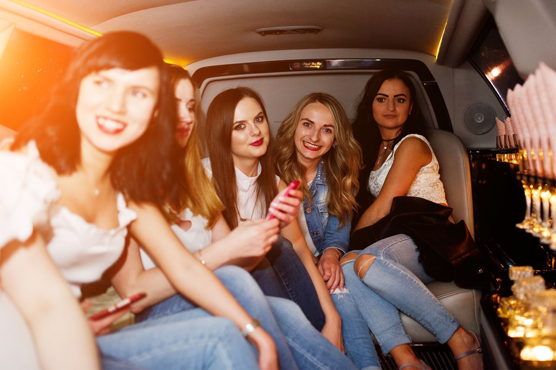 Five women smiling and looking at the camera inside a limousine.