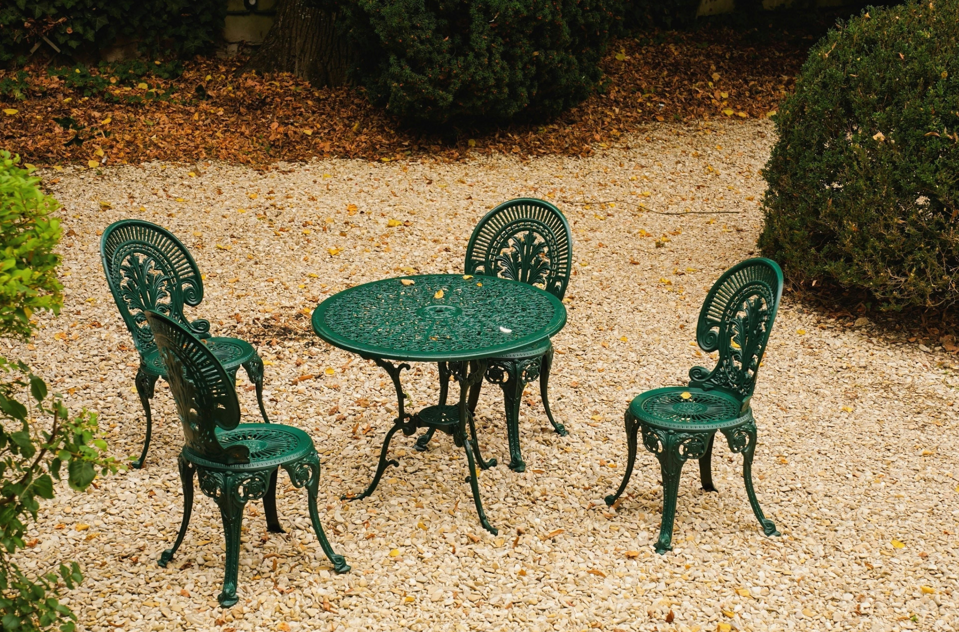 Green cast iron patio table and chairs on a gravel patio.