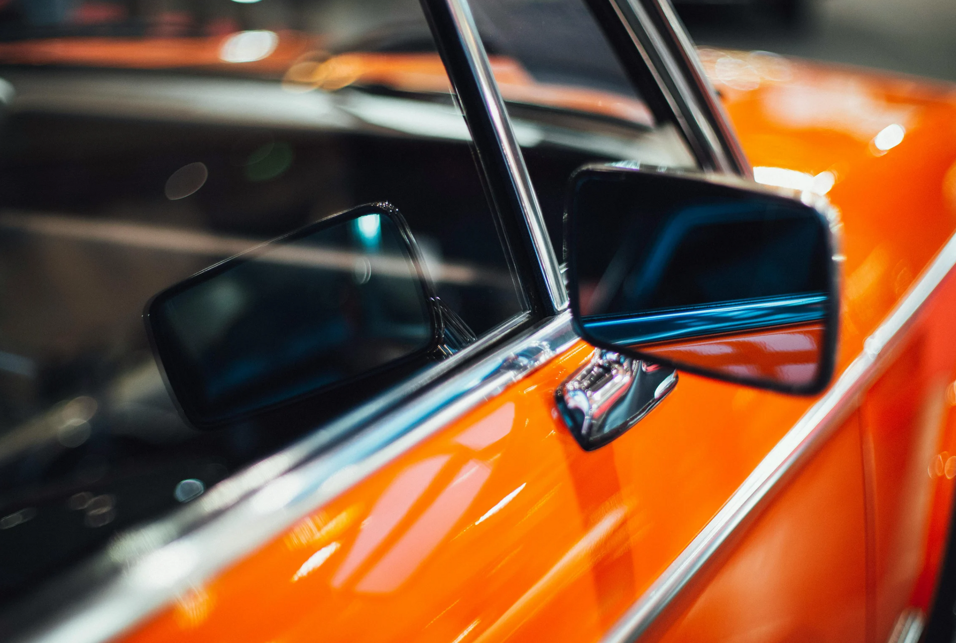 Close-up of orange vintage car body, chrome trim, and side mirrors.