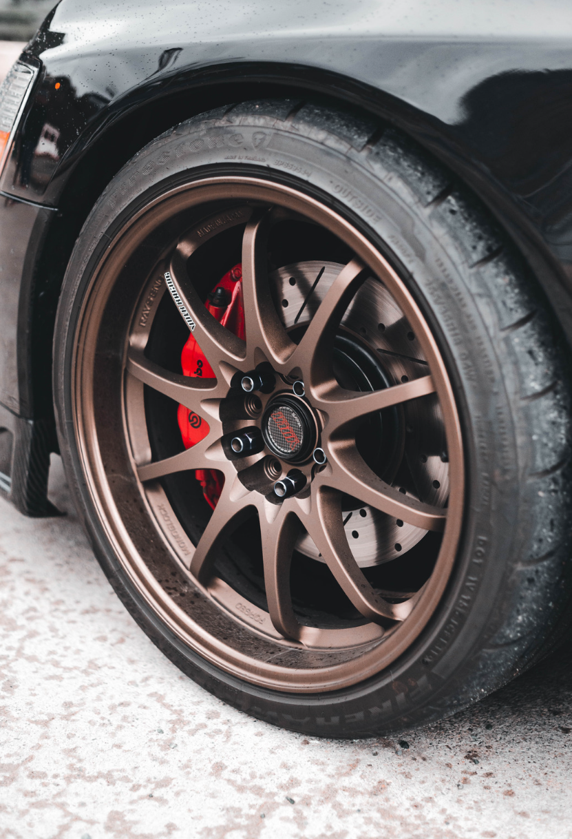 Black car's bronze wheel. Red brake calipers visible. Close-up shot, wet pavement.