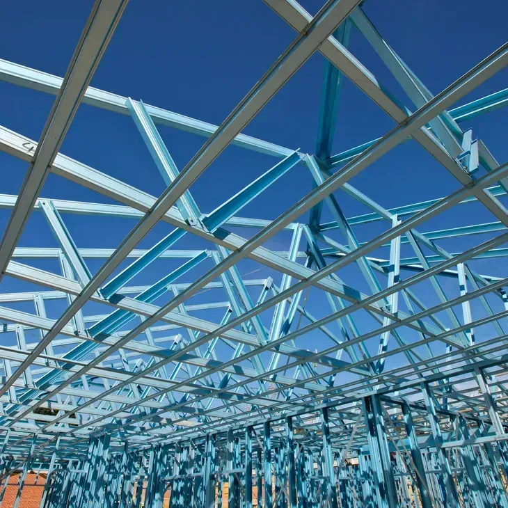 Blue steel frame of a building under construction, set against a bright blue sky.