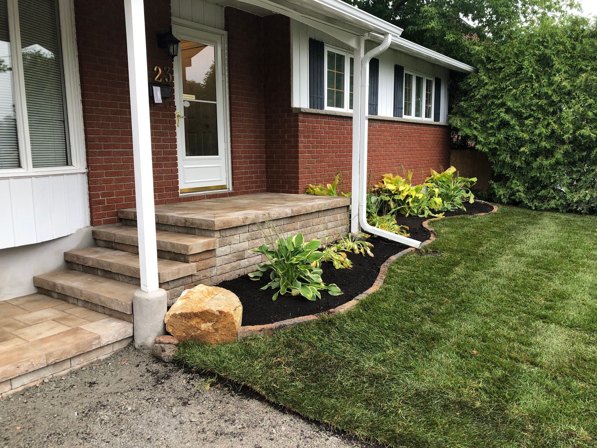 A brick house with a porch and steps and a lush green lawn.