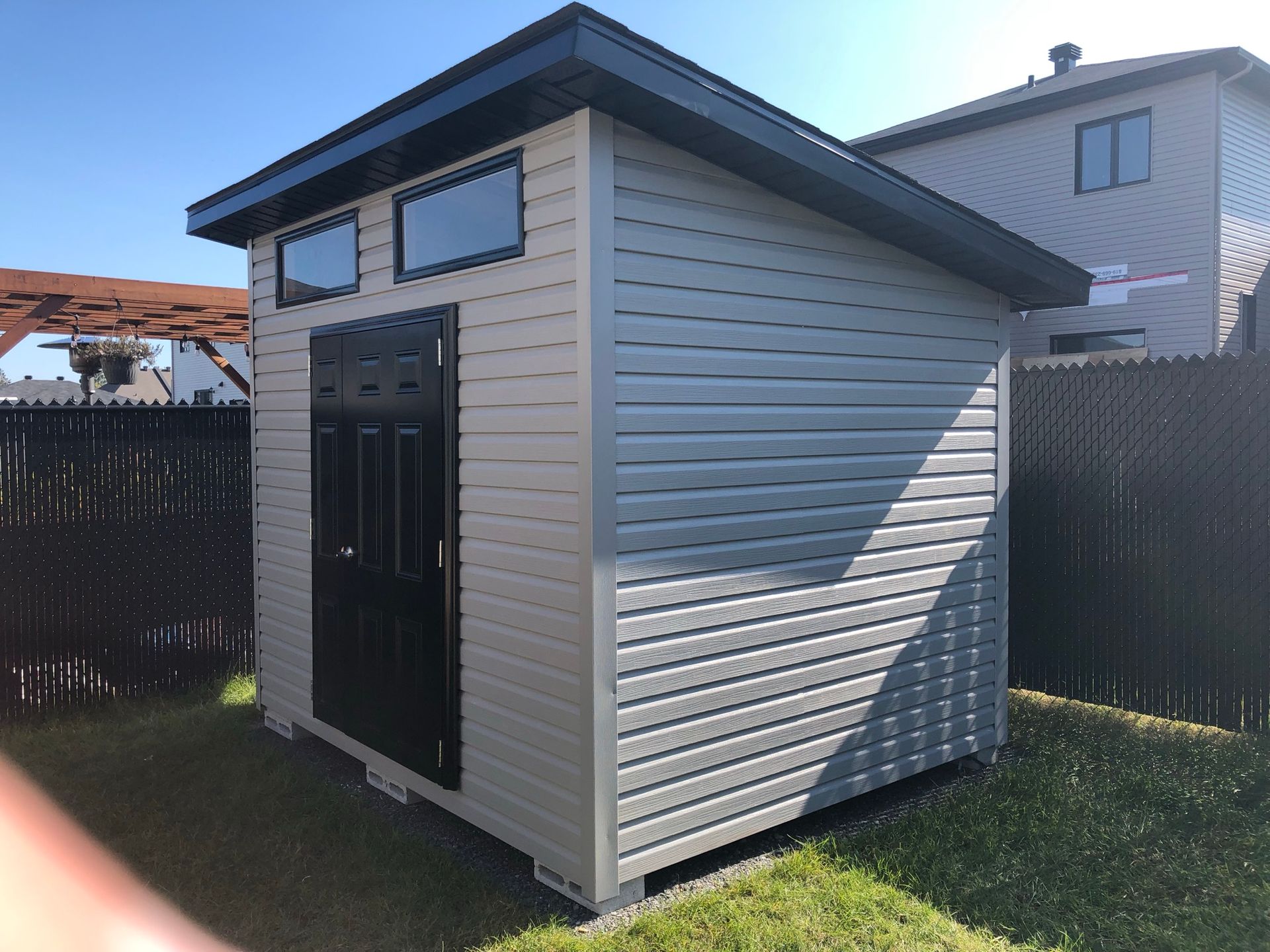 A small shed in a backyard with a fence and a house in the background