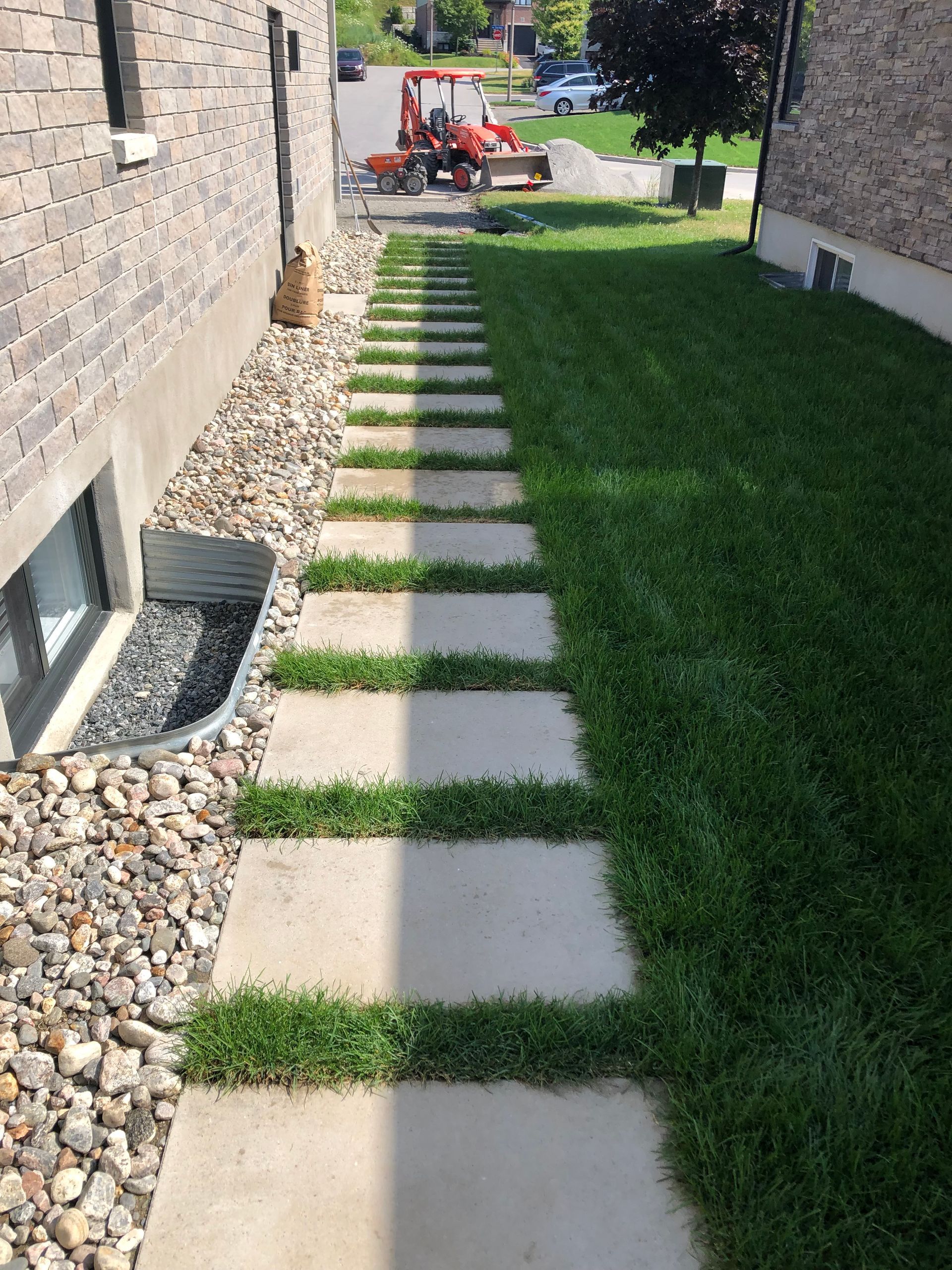 A stone walkway leading to a house with a tractor in the background
