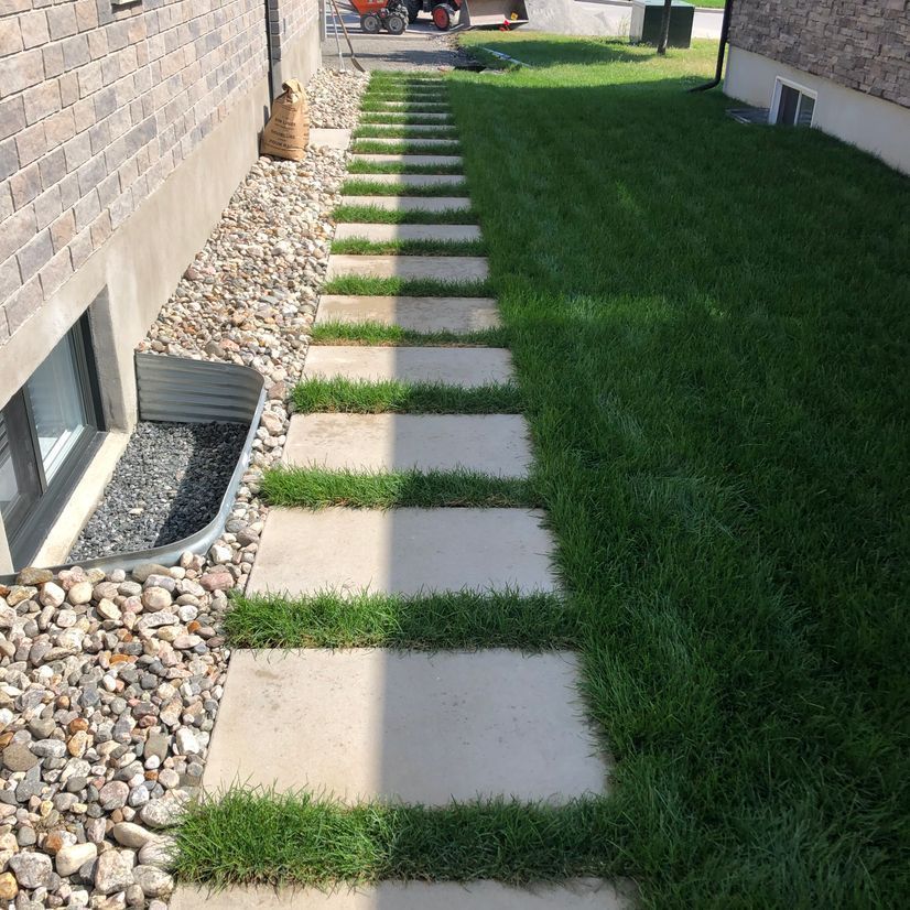 Une allée en pierre menant à une pelouse verte luxuriante à côté d'un bâtiment en briques.