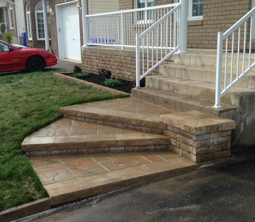 Une voiture rouge est garée devant une maison avec des escaliers et une rampe.