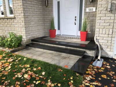 A front porch of a brick house with steps and potted plants.