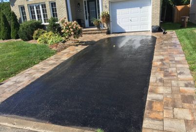 A black driveway with a brick walkway leading to a garage.