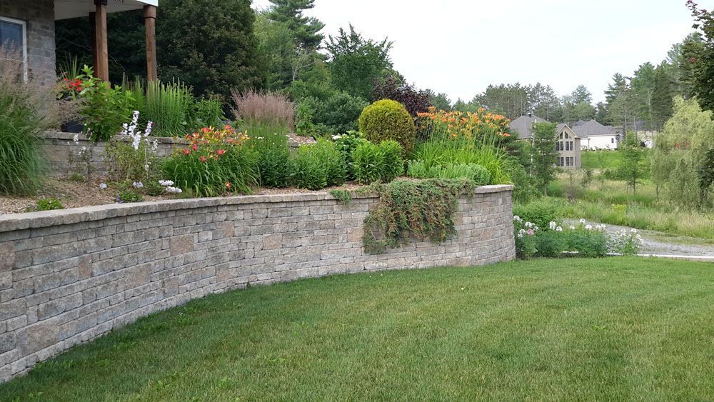 Un mur de pierre entoure une pelouse verte luxuriante devant une maison.