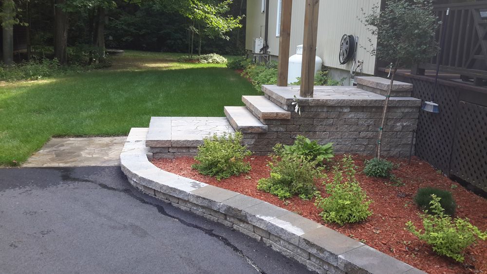 Une allée avec un mur de pierre et des marches menant à une maison.