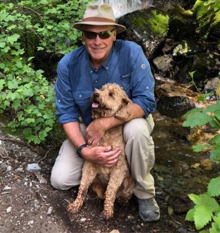 A man in a hat is kneeling down next to a dog.