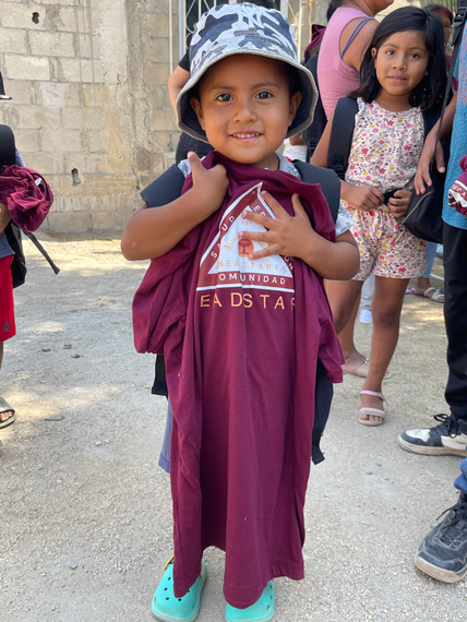 A little boy wearing a hat and holding a t-shirt 