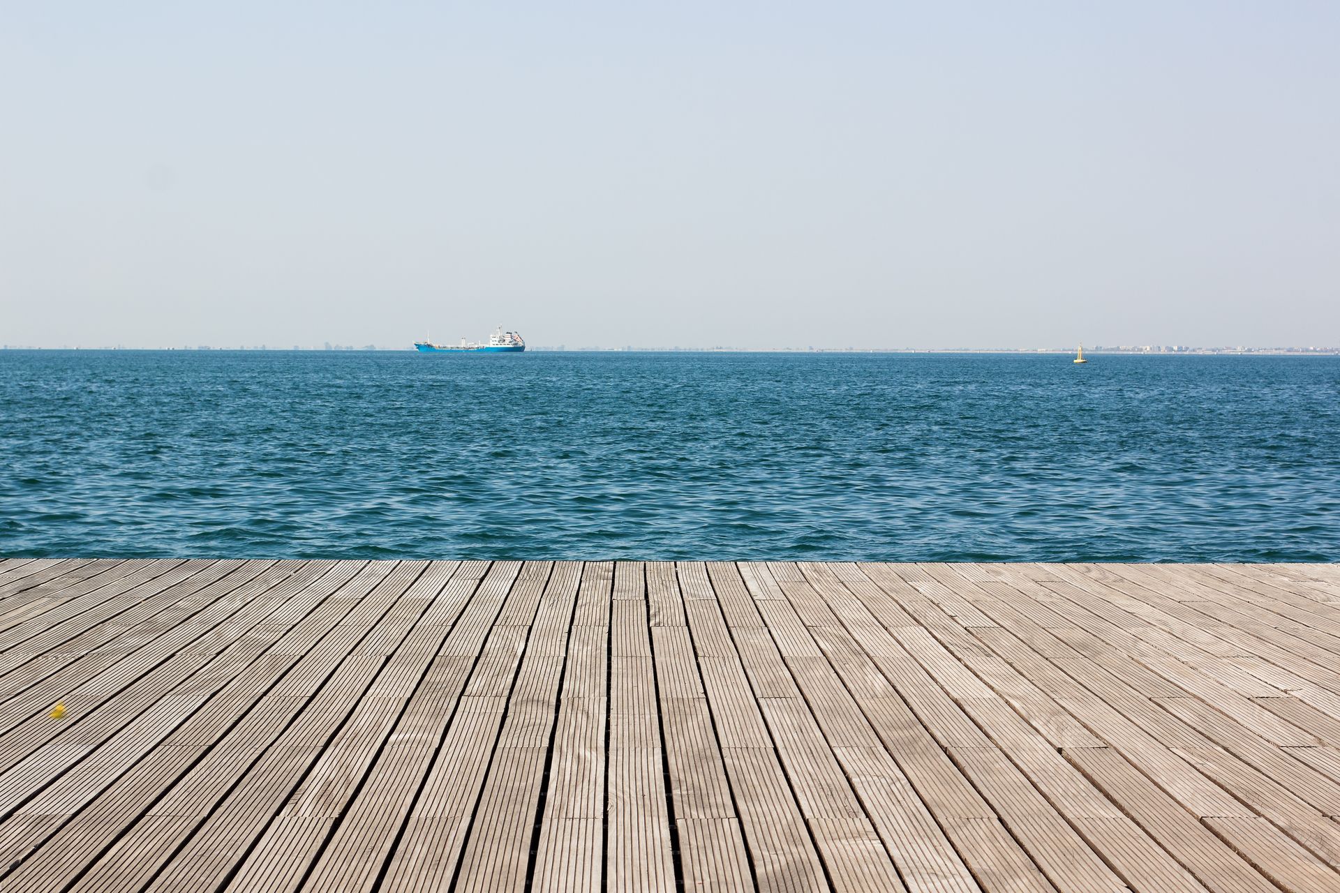 An empty wooden pier overlooking the ocean with a boat in the distance.