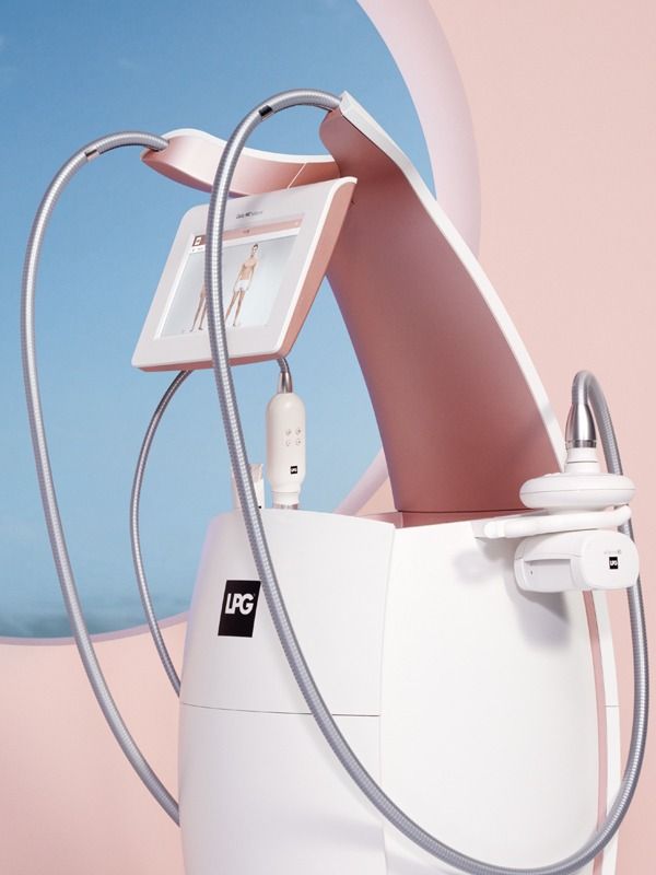 White and pink LPG medical device with touchscreen, hoses, and applicator, in a soft pastel setting.