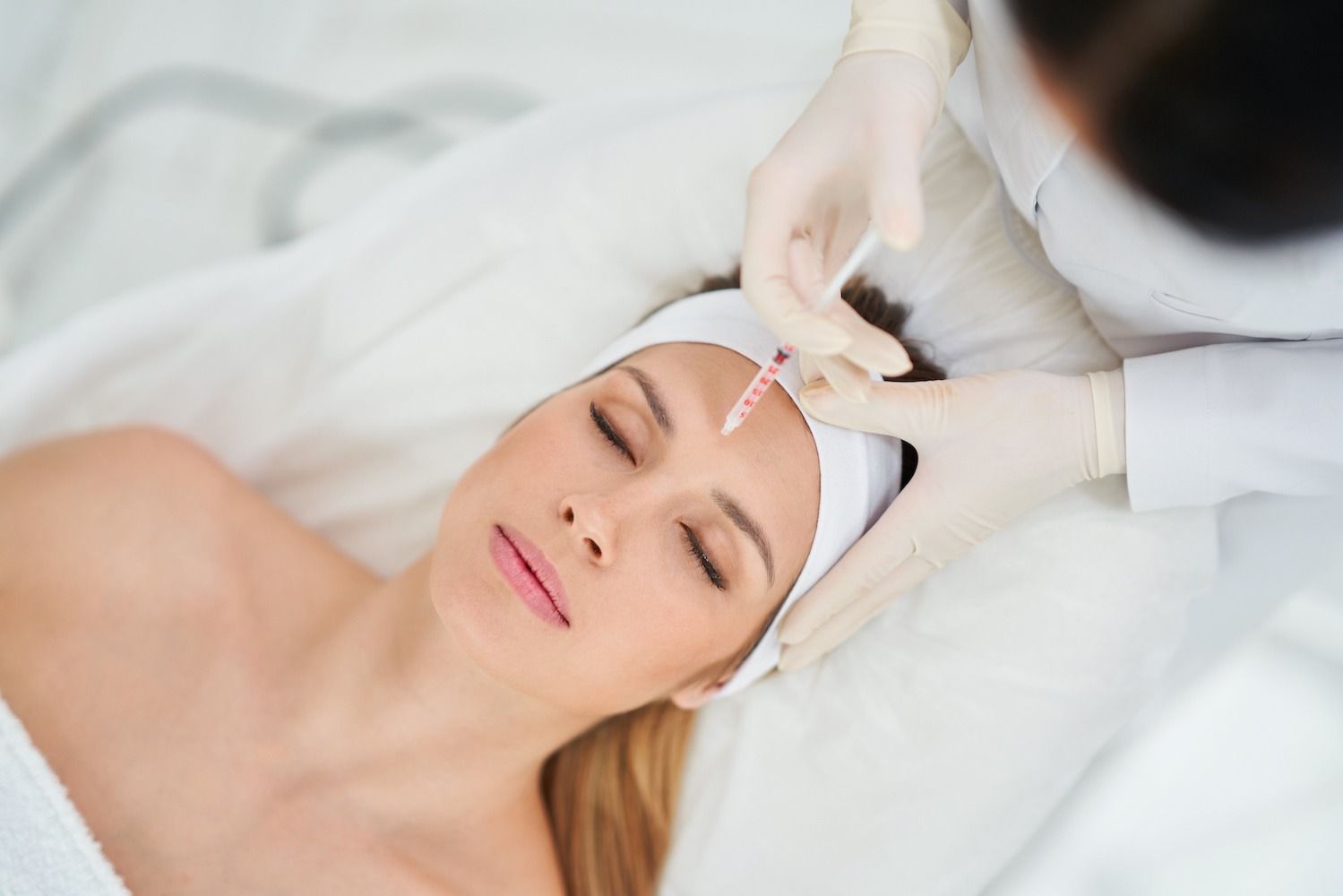 Woman receiving an injection in her forehead from someone wearing gloves in a medical setting.
