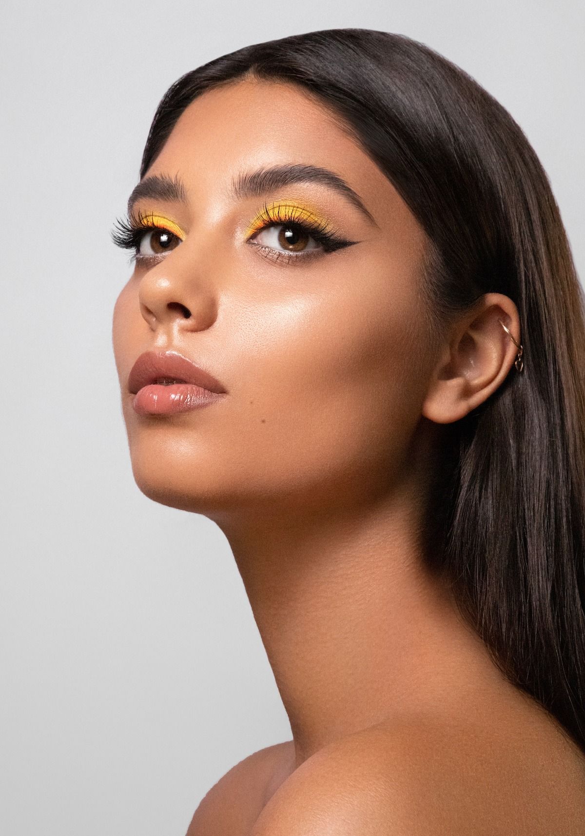 Woman with dark hair, wearing yellow eyeshadow and winged eyeliner, looking to the side.