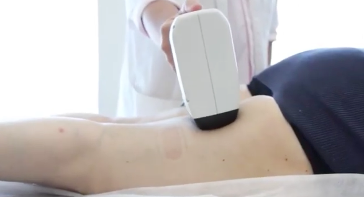 Person receiving treatment on their lower back with a handheld device; white setting.