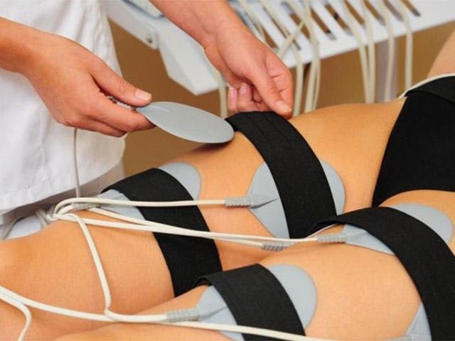 Person receiving electrotherapy on their thighs, with pads attached by straps.