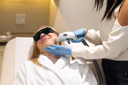 Woman receiving laser facial treatment. A technician holds the laser device.