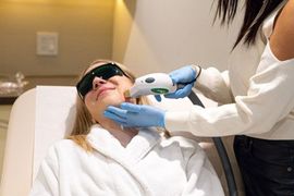 Woman receiving laser facial treatment. A technician holds the laser device.
