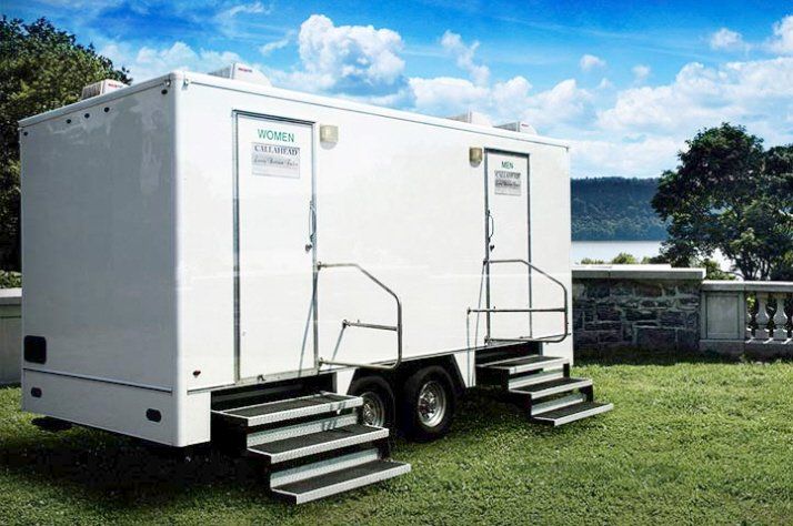 a white trailer with two toilets on it is parked in a grassy field .