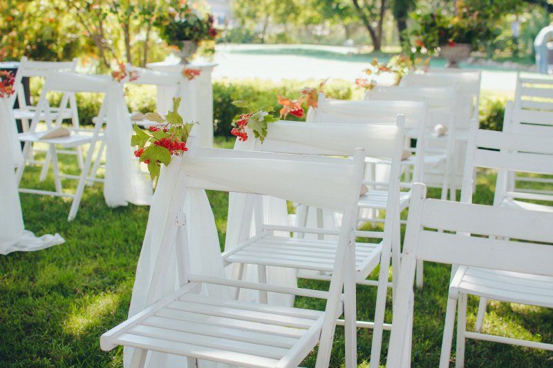 a row of white folding chairs with decorations on the backs