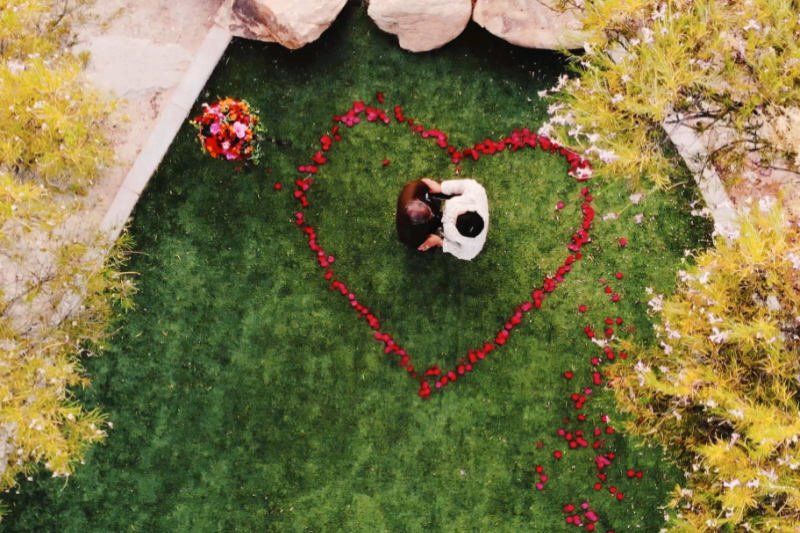 Wedding celebration romantic proposal with couple standing within roses forming a heart from above