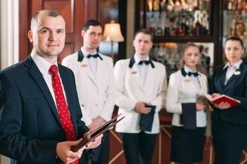 a man in a suit and tie is standing in front of a group of waiters and waitresses.