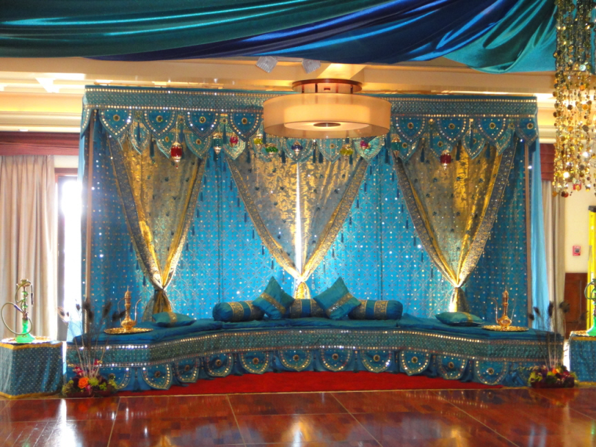a mandap stage with blue and gold curtains and pillows
