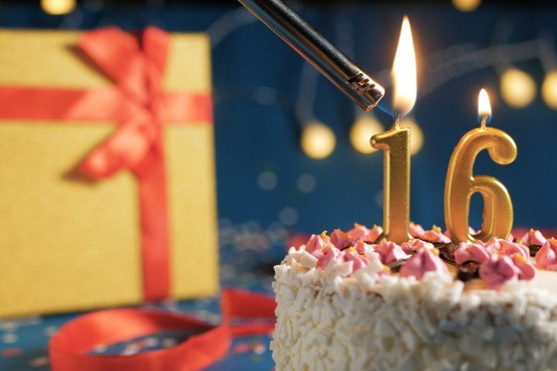 Image showing wrapped gift and birthday cake with numeric candles being lit showing  16