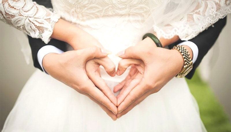 Bride and groom holding hands forming a heart hand gesture