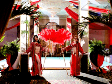 two belly dancers are standing in front of a large red fan.
