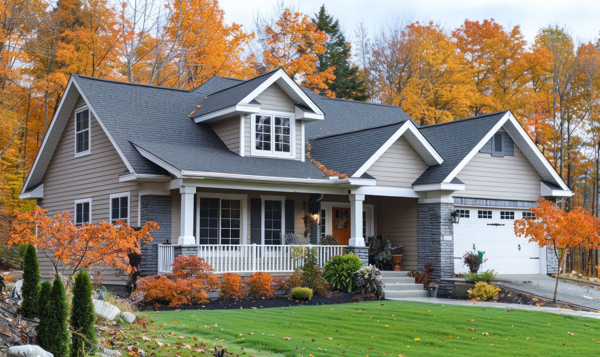 House with tan siding, gray roof, and stone accents, surrounded by autumn trees.