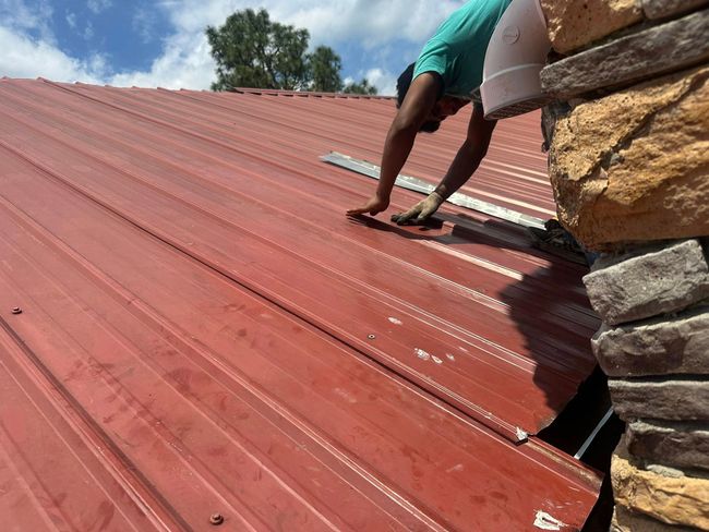 A man is working on a red roof next to a stone wall.