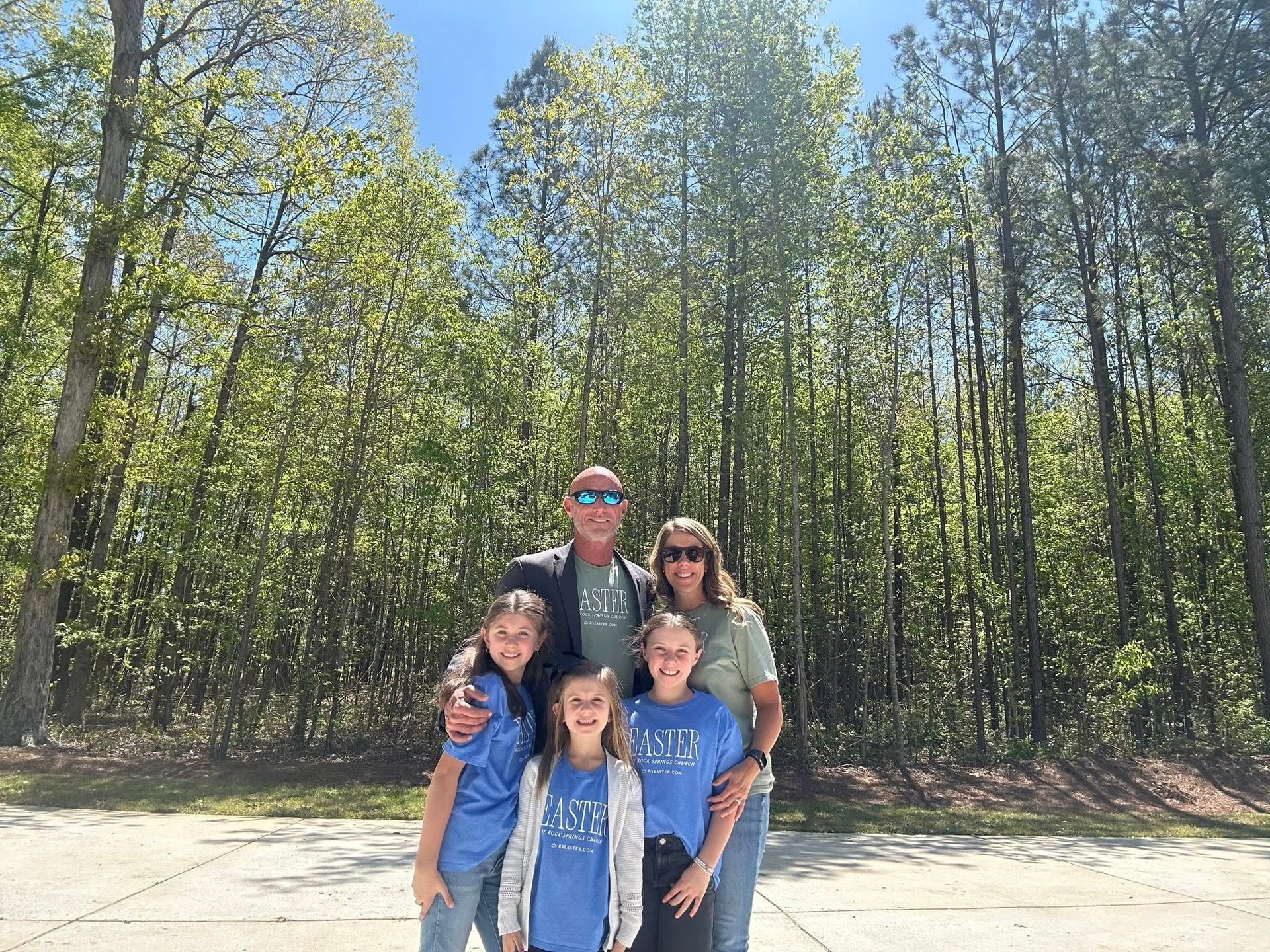 A family is posing for a picture in front of a forest.