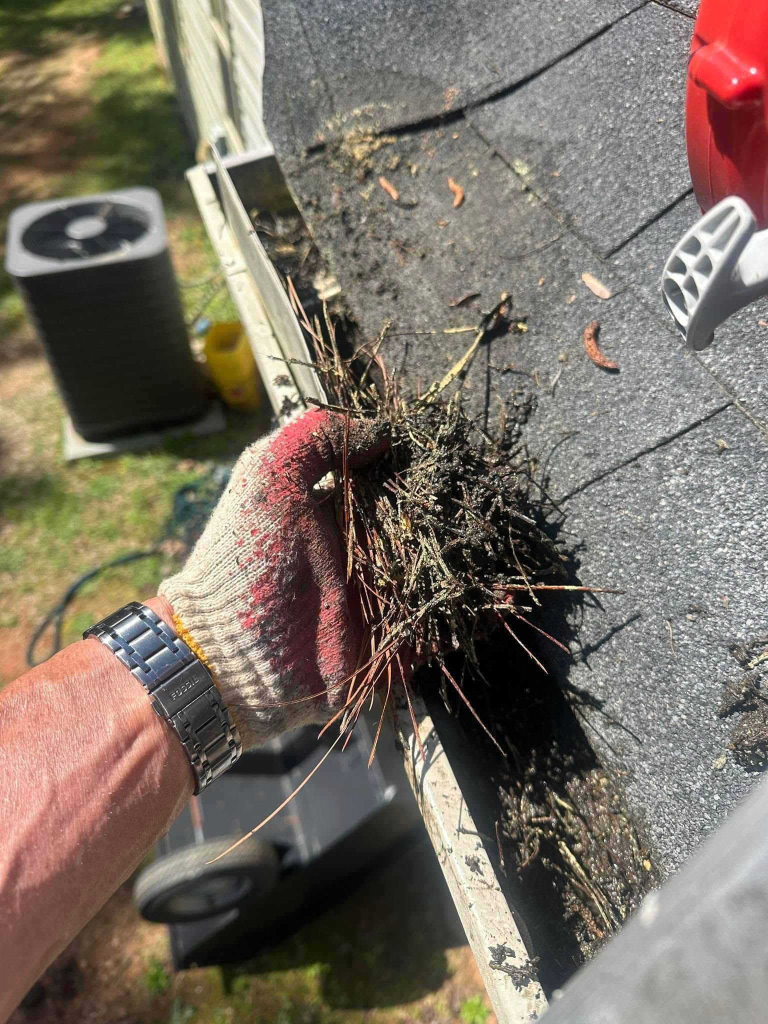 A person wearing gloves is cleaning a gutter on a roof.