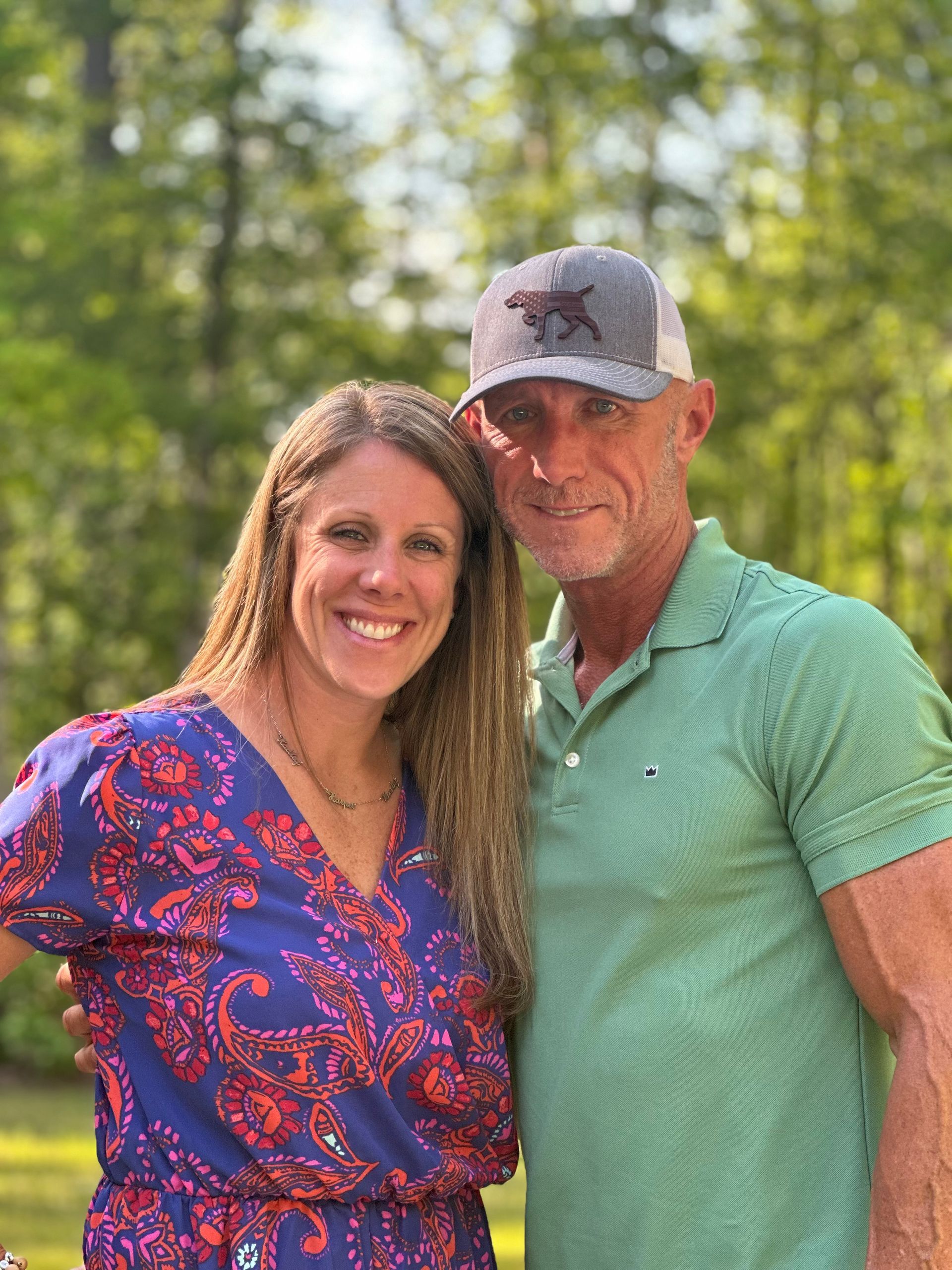 A man and a woman are posing for a picture in front of trees.