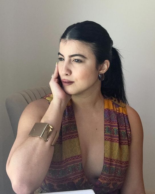A woman is sitting at a desk with a laptop and a vase of flowers.