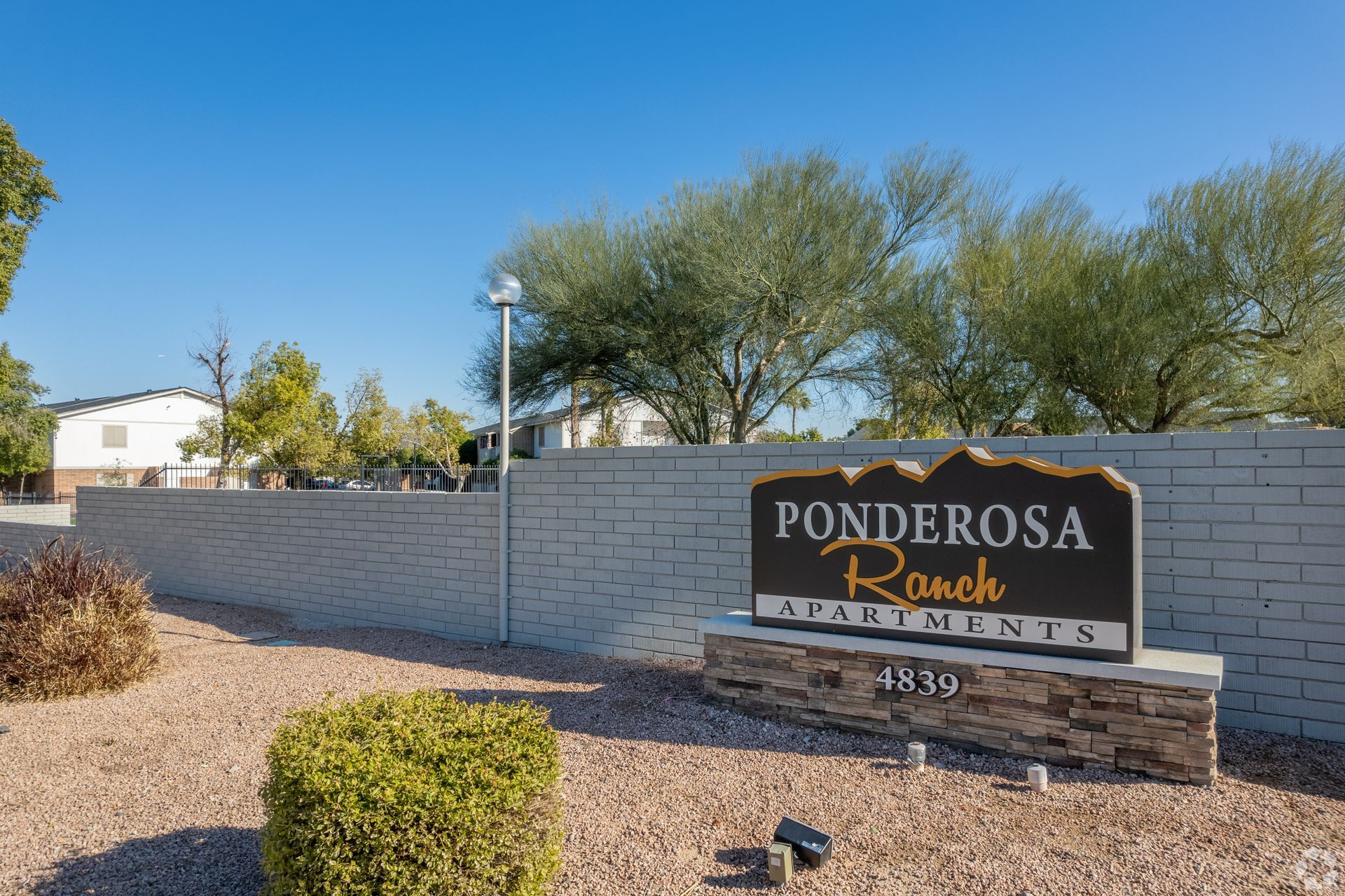 Sign for Ponderosa Ranch Apartments, on a brick wall, with landscaping and blue sky.