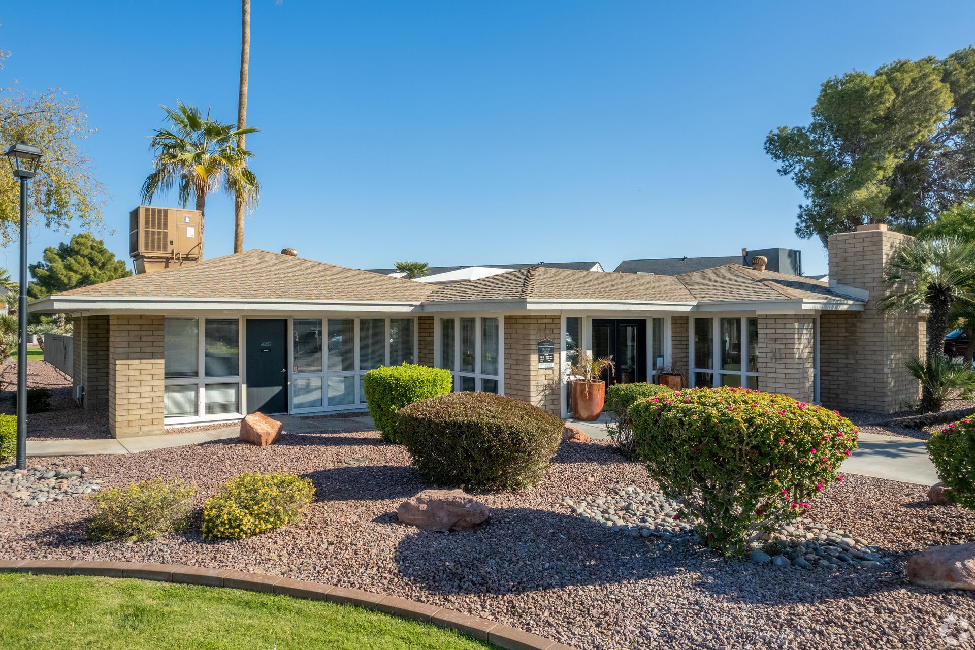 Single-story brick home with bushes and a rock garden under a blue sky.
